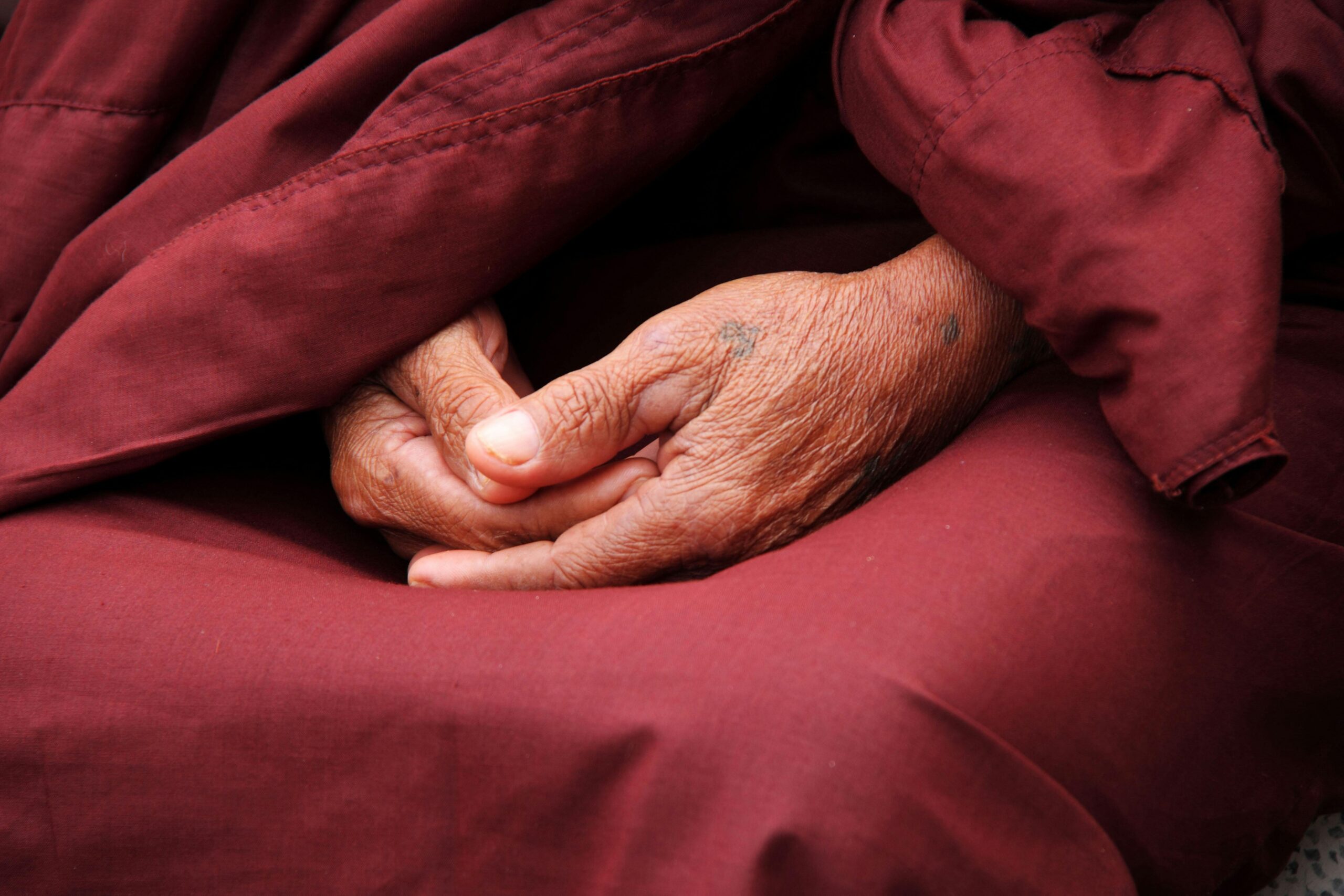 Close-up of a monk's hands in prayer, wrapped in maroon robe, symbolizing peace and spirituality.